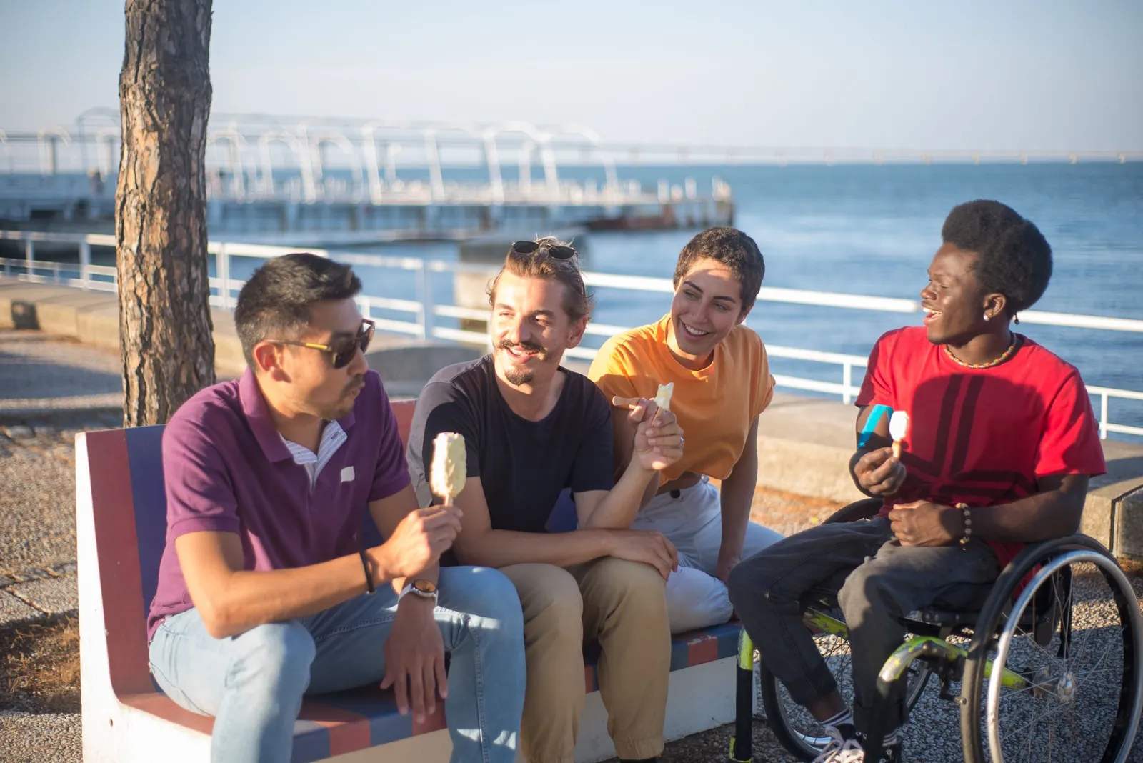 Friends eat ice cream together on a bench by the water