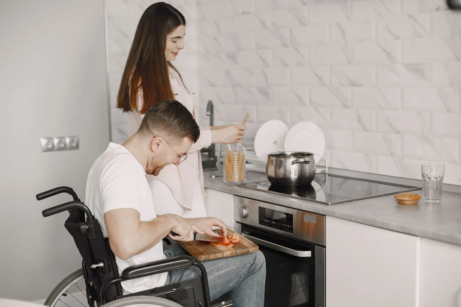 A man using a wheelchair and a support person prepare a meal together in a kitchen