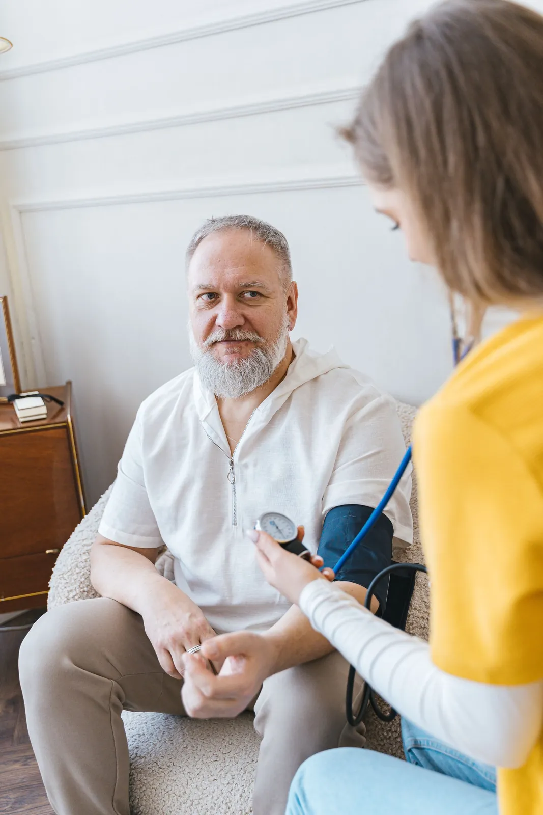 A nurse takes an older man's blood pressure in his living room