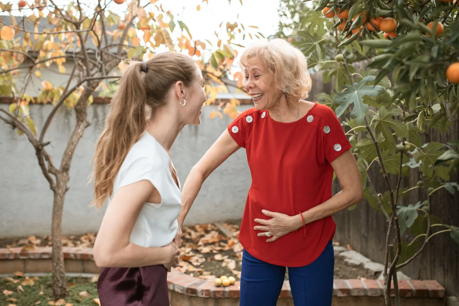 Two women laugh together under fruit trees in a garden