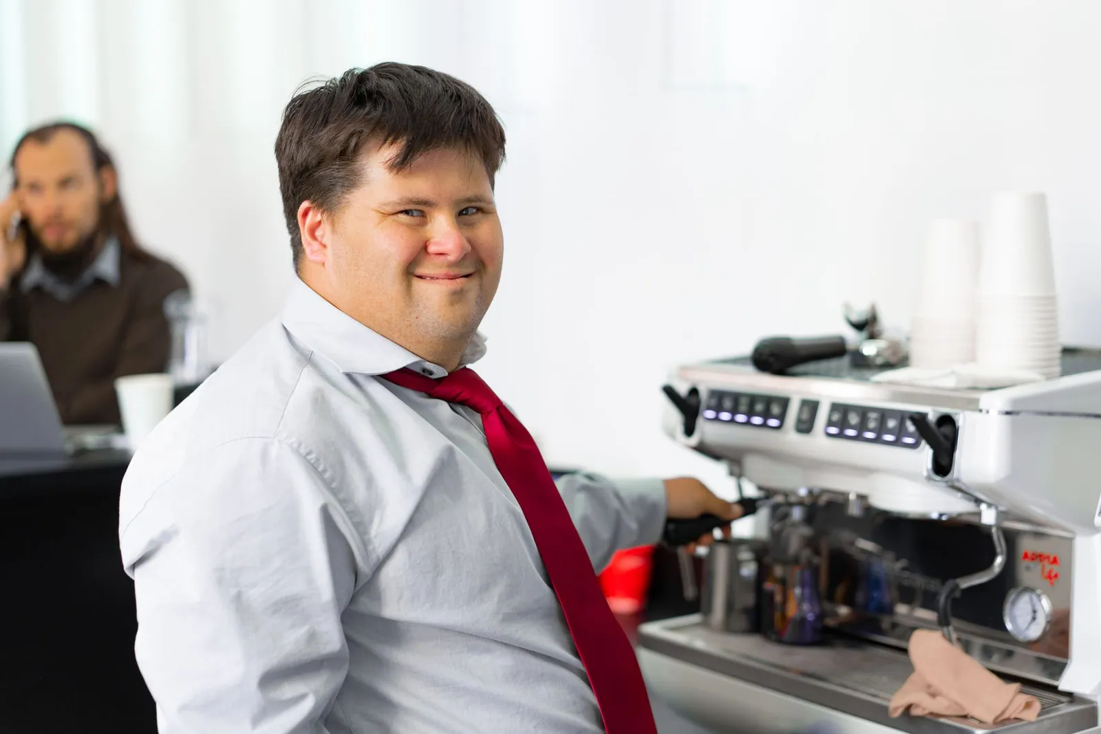 A young man smiles while making coffee at a café coffee machine