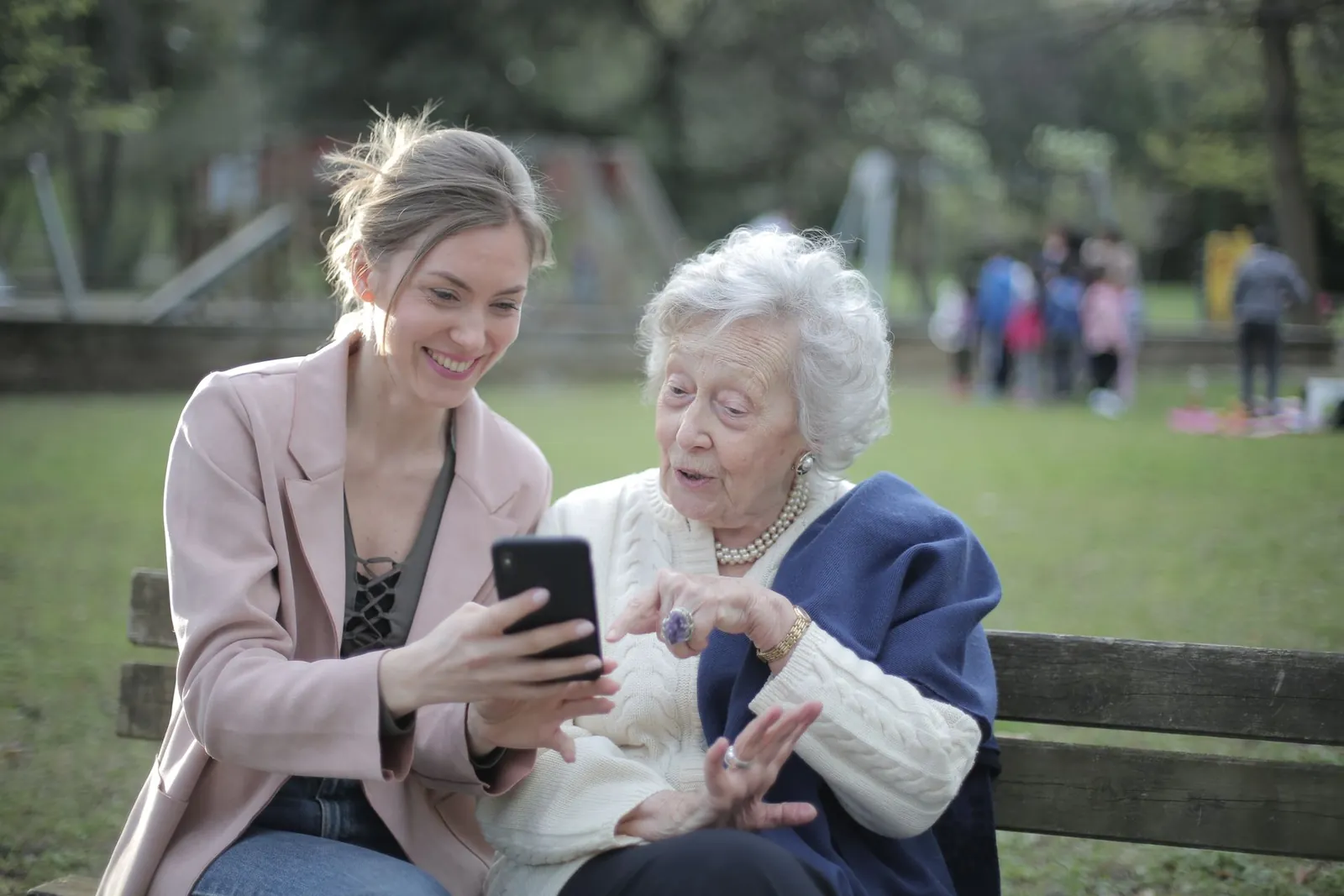 Two women smile while finding answers on a phone in the park