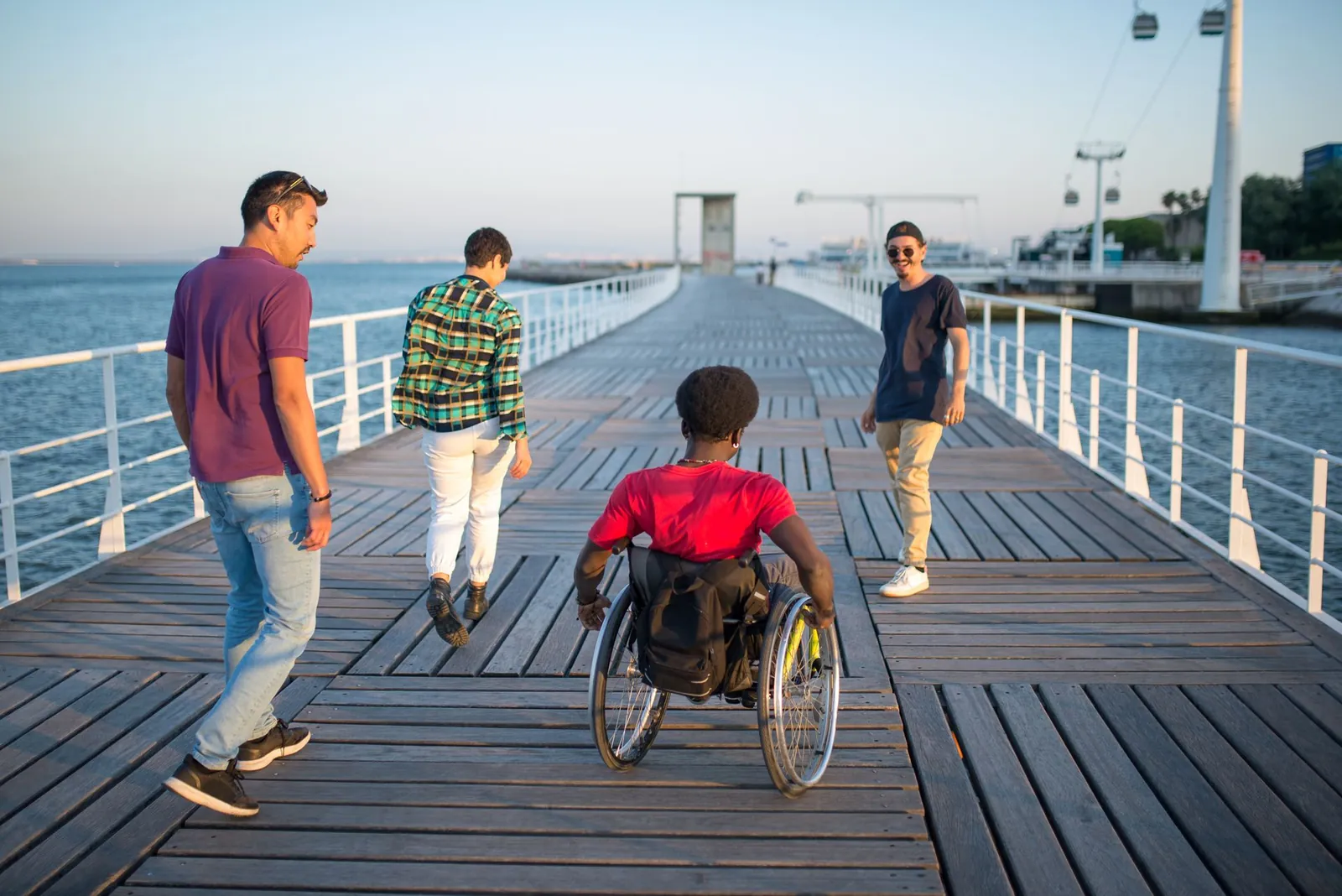 Friends stroll along a seaside boardwalk together, one of them using a wheelchair