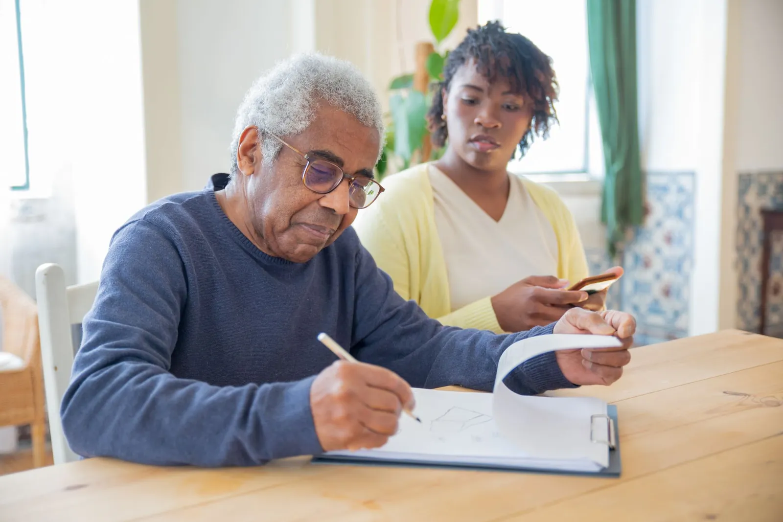 A man and a support person work through paperwork together at a table