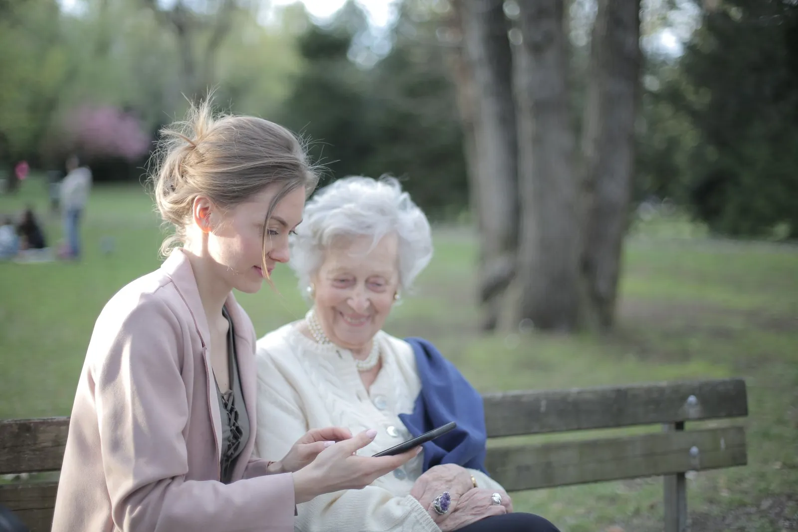 Two women practise using a smartphone together on a park bench