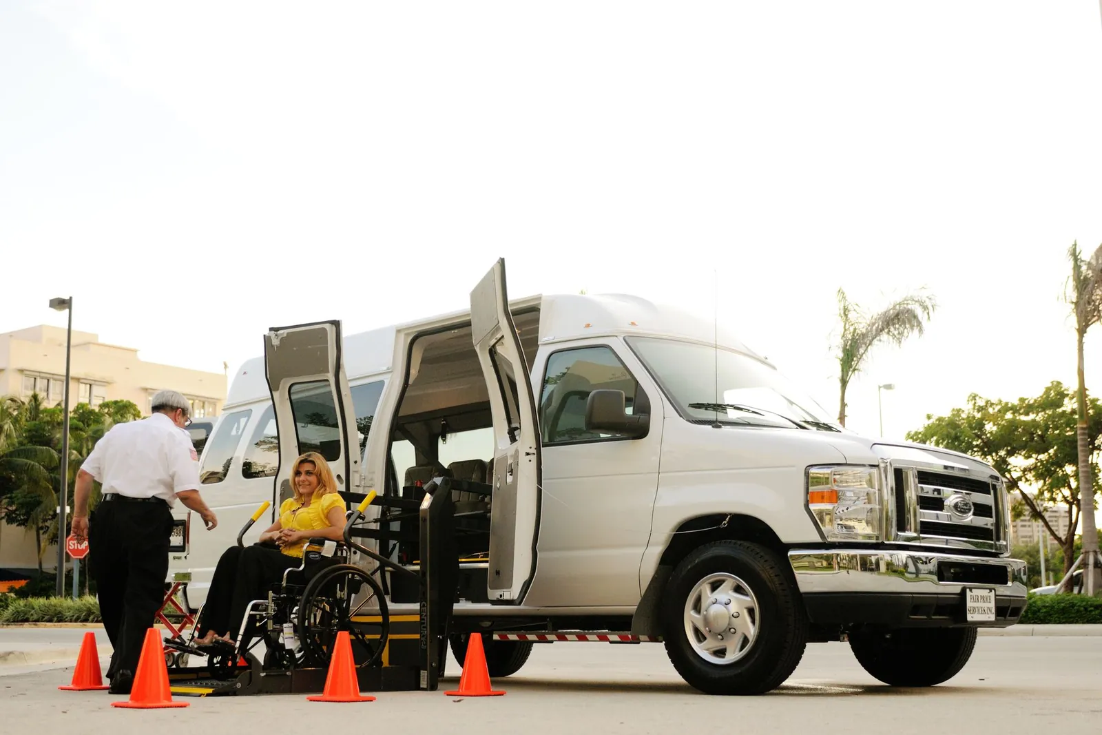 A driver assists a person in a wheelchair onto a van's wheelchair lift